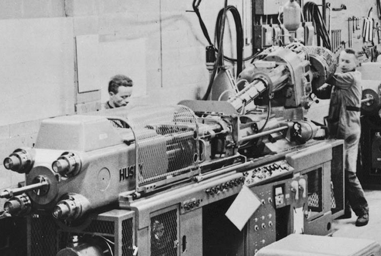 A historical photo of Husky technicians running an injection molding system